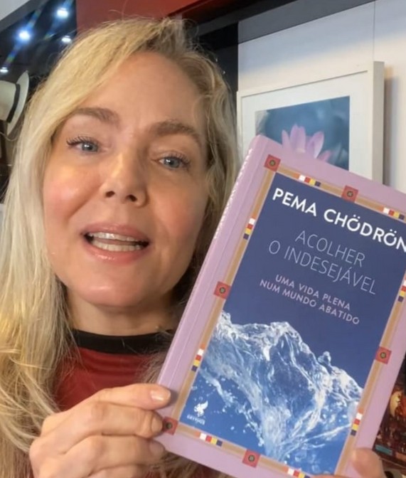 Foto de Celina Figueiredo apresentando uma capa de livro de Pema Chödrön chamado Acolher o Indesejável