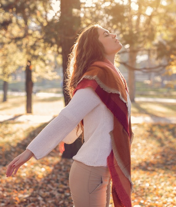 Mulher com os olhos fechados em um bosque no outono, sentindo a natureza a seu redor